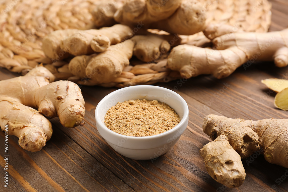 Fresh ginger roots and bowl with dried powder on wooden background