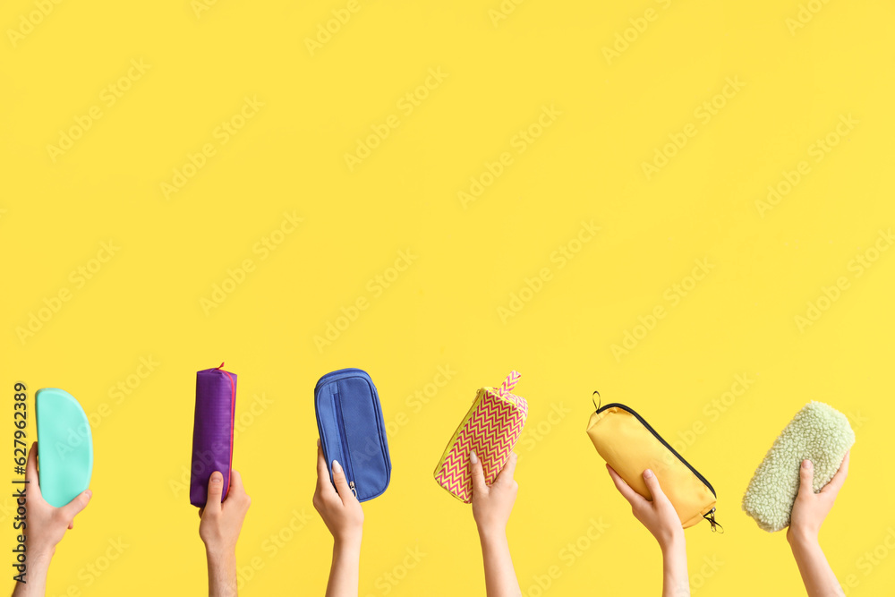 Hands with pencil cases on yellow background