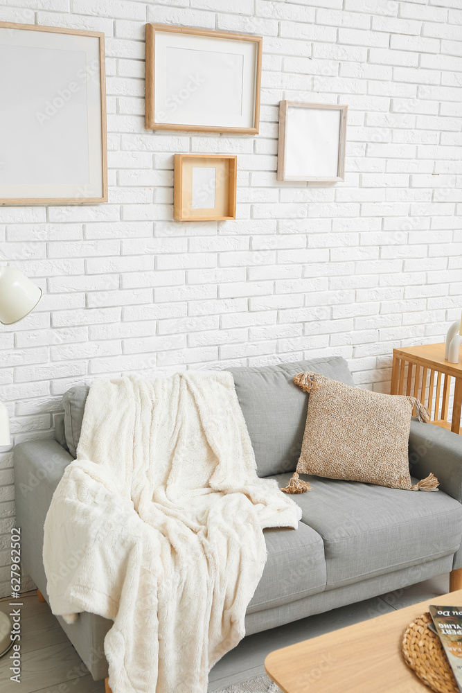 Interior of stylish living room with sofa and blank frames on white brick wall