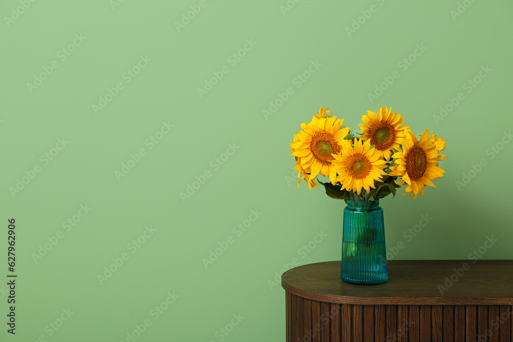 Vase with beautiful sunflowers on table near green wall in room