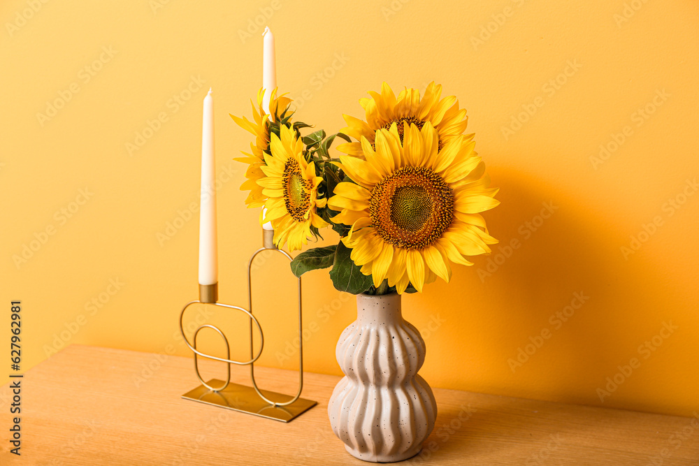 Vase with beautiful sunflowers and candles on table near orange wall in room, closeup