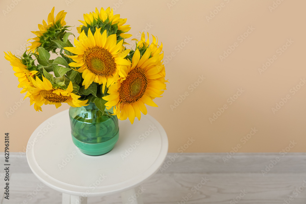 Vase with beautiful sunflowers on table near beige wall in room, closeup