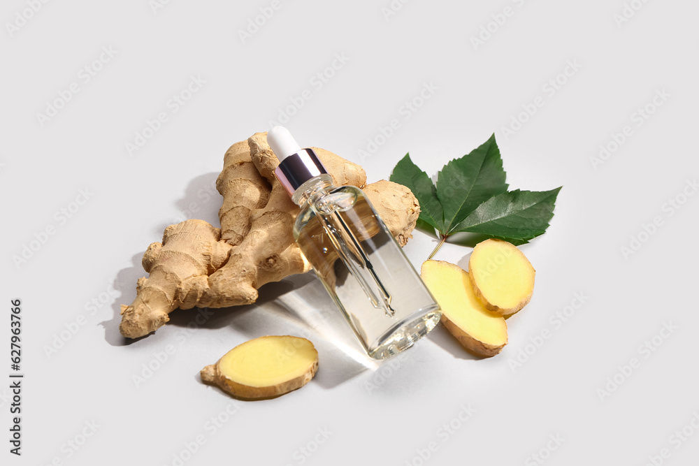 Bottle of ginger cosmetic oil and leaves on grey background