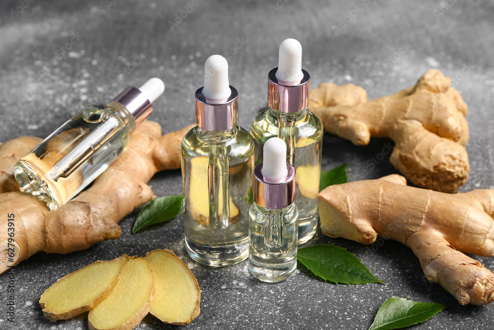 Bottles of ginger cosmetic oil and leaves on grey table