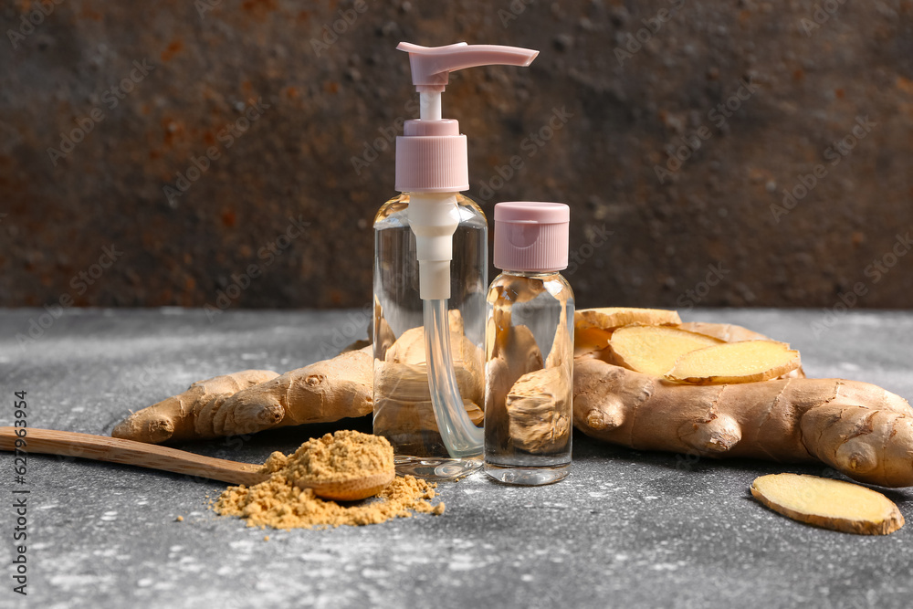 Bottles of ginger cosmetic oil and wooden spoon with dried powder on grey table