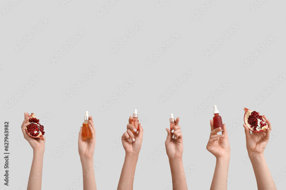 Female hands holding bottles with cosmetic products and pomegranate on grey background