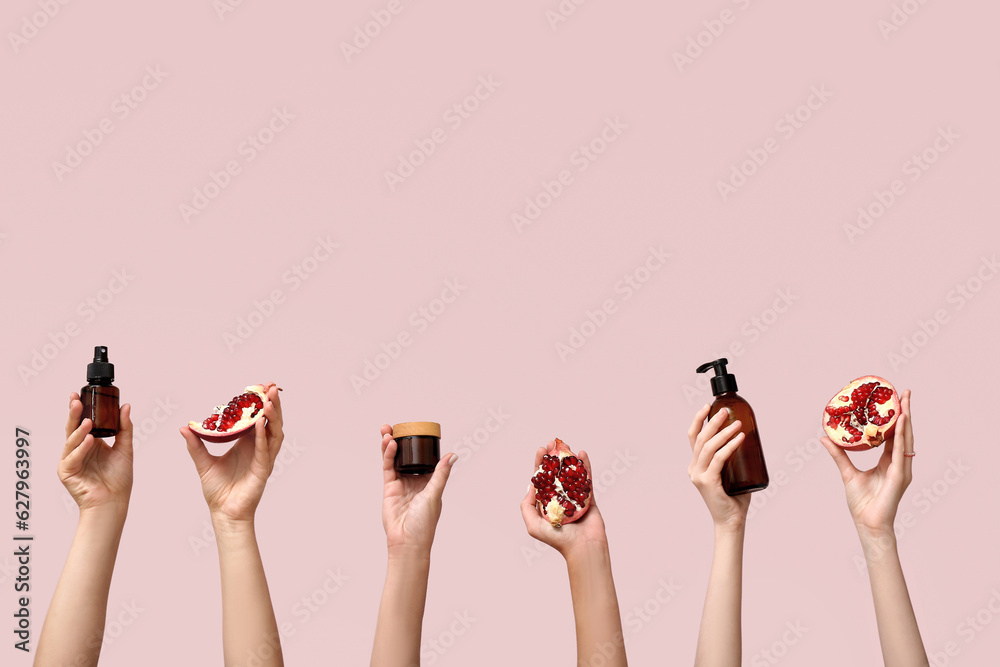 Female hands holding cosmetic products and pomegranate on pink background