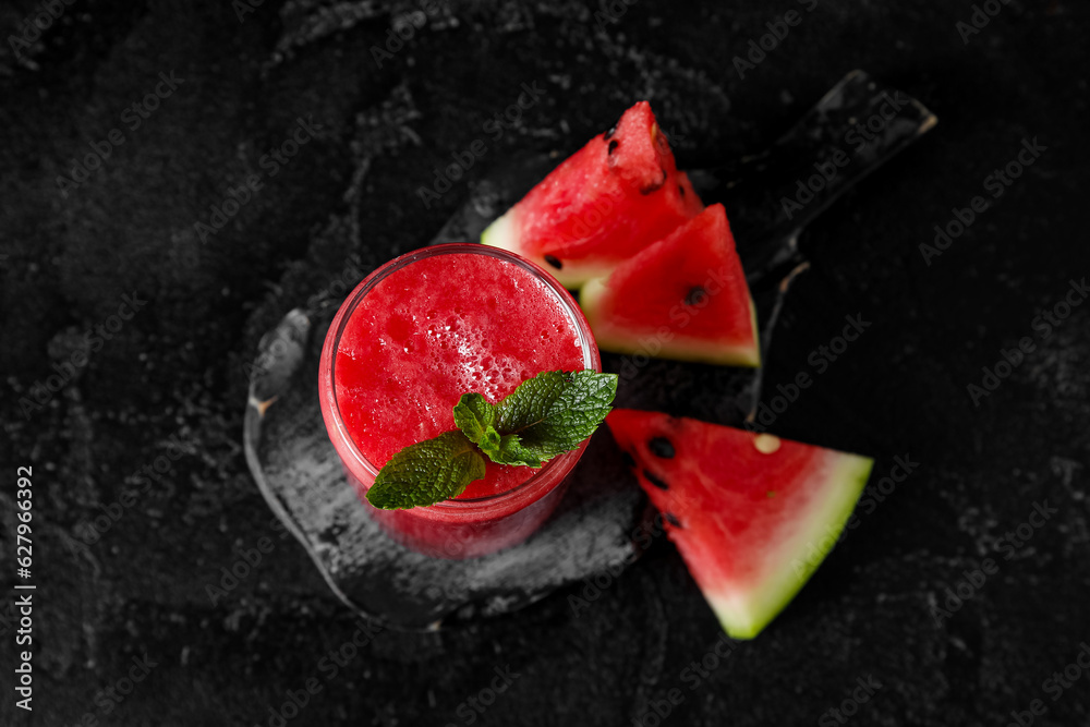 Board with glass of tasty watermelon juice and mint on black background