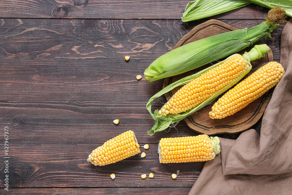 Board with fresh corn cobs on dark wooden table