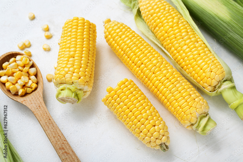 Fresh corn cobs and wooden spoon with kernels on white table