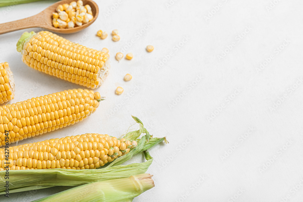 Fresh corn cobs and wooden spoon with kernels on white table