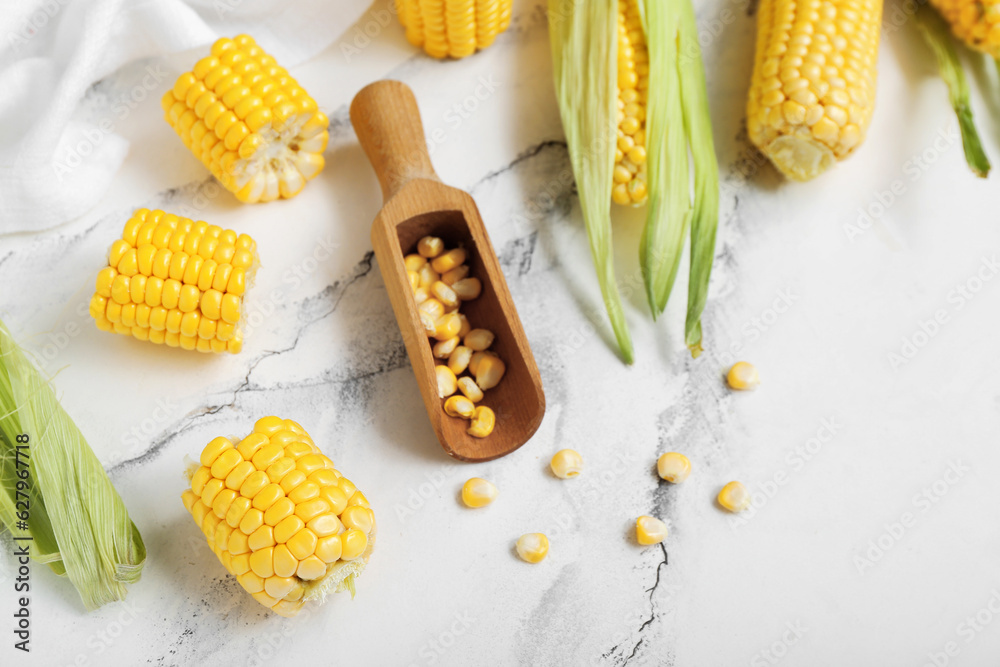 Fresh corn cobs and wooden scoop with kernels on white marble table