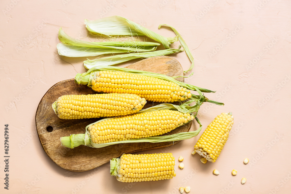 Wooden board with fresh corn cobs on beige table