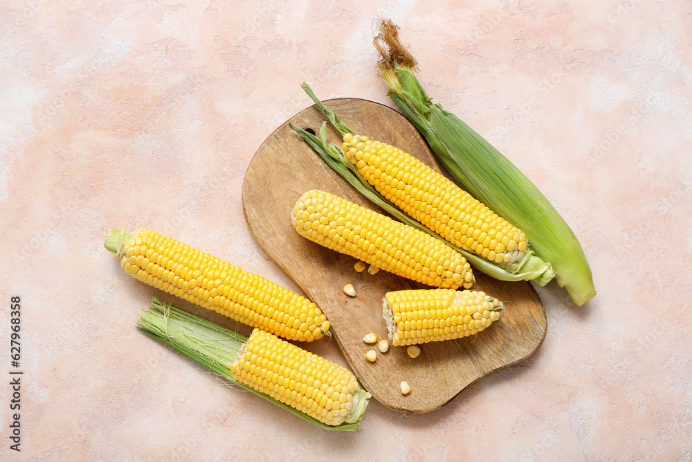 Wooden board with fresh corn cobs on beige table