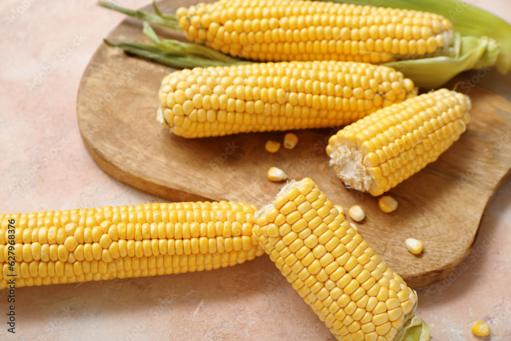 Wooden board with fresh corn cobs on beige table, closeup