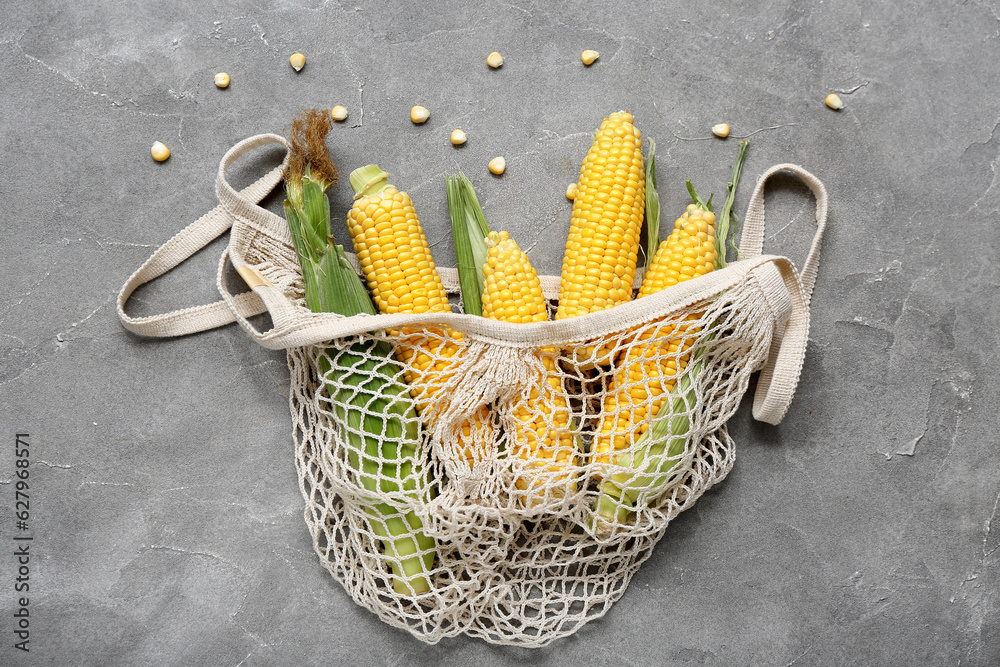 Mesh bag with fresh corn cobs on grey table