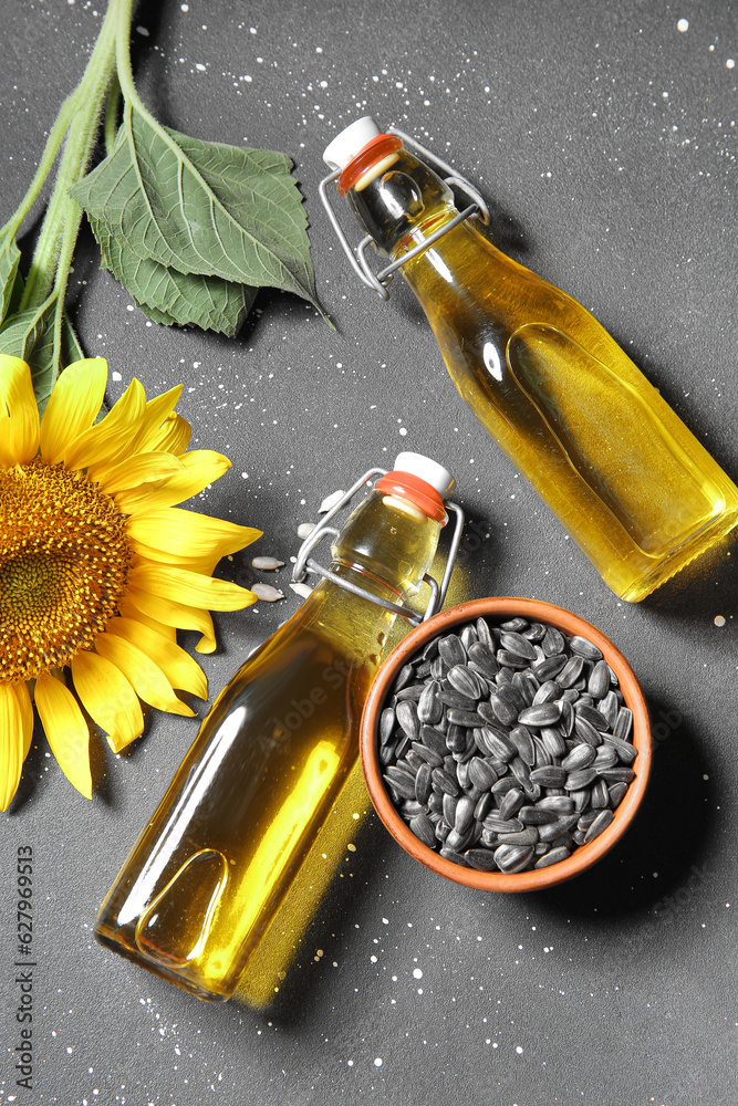 Bottles of sunflower oil and bowl with seeds on black background