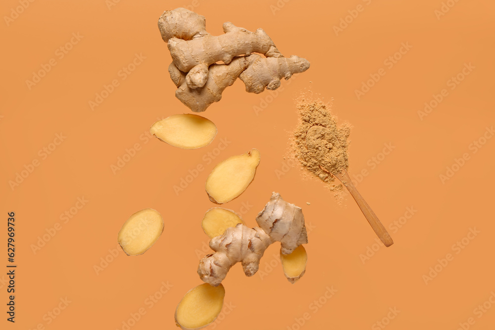 Flying slices of fresh ginger root and wooden spoon with dried powder on orange background