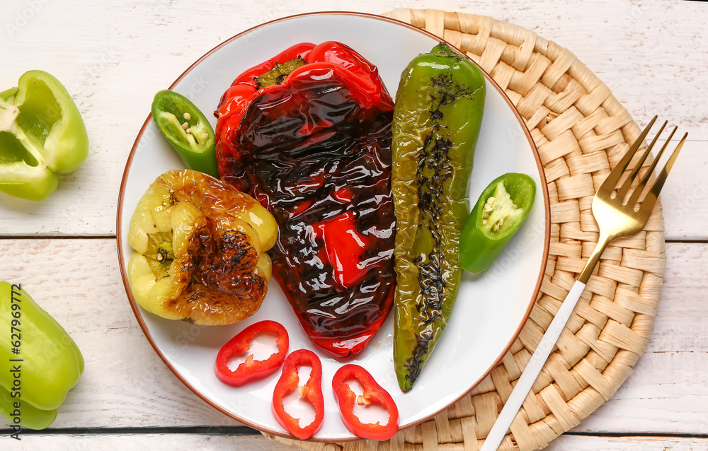 Plate with different grilled peppers on light wooden background