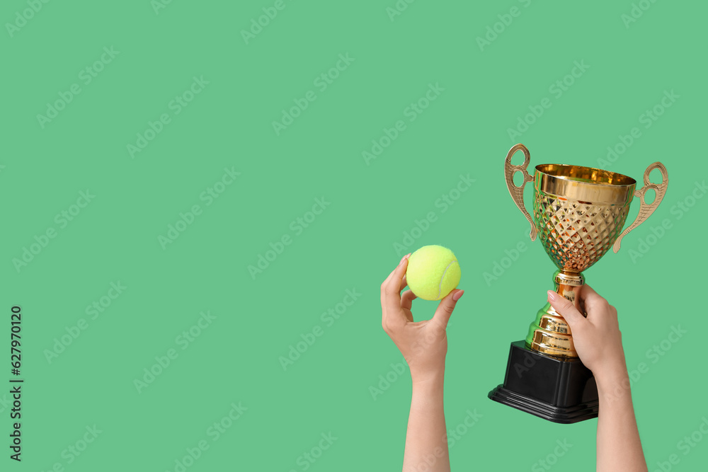 Female hands with gold cup and tennis ball on green background