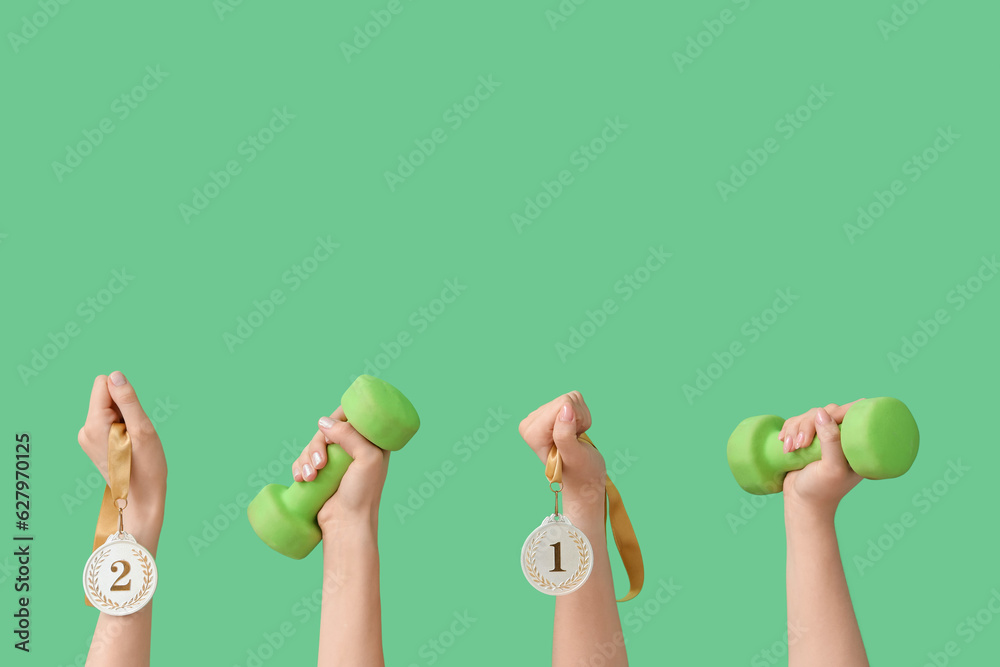 Female hands with dumbbells and medals on green background