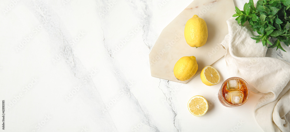 Glass of ice tea, mint and lemons on white marble background with space for text, top view