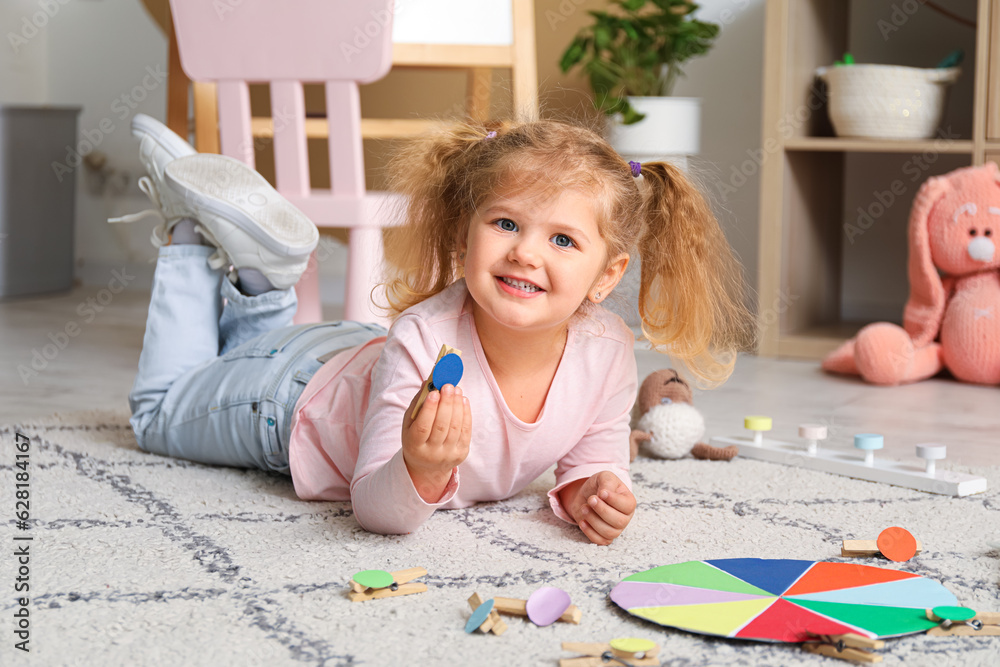 Cute little girl playing matching game with clothespins on floor at home