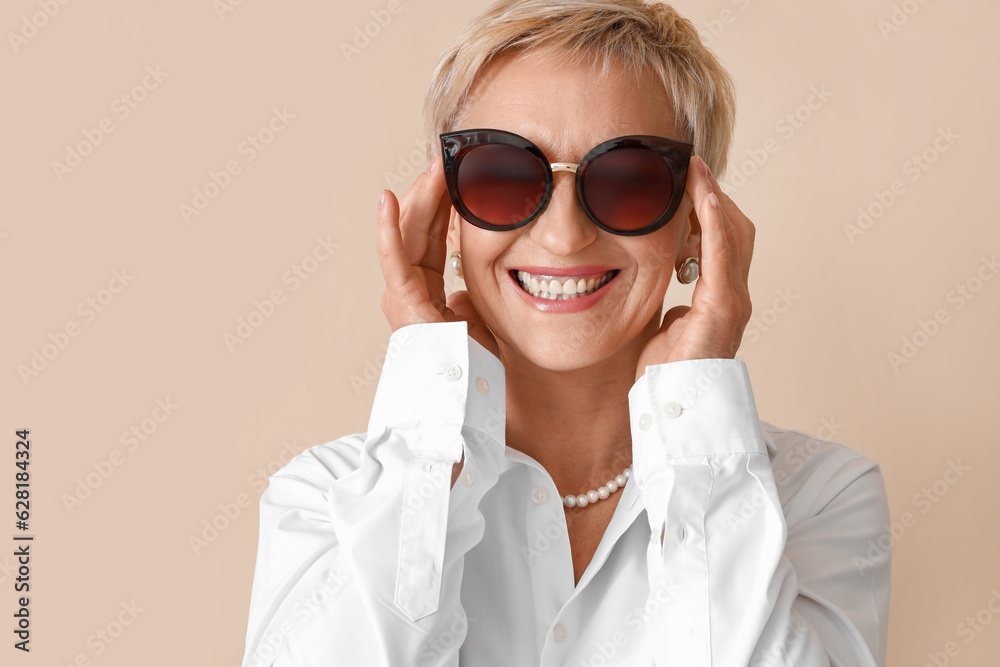 Beautiful mature woman in sunglasses on beige background, closeup