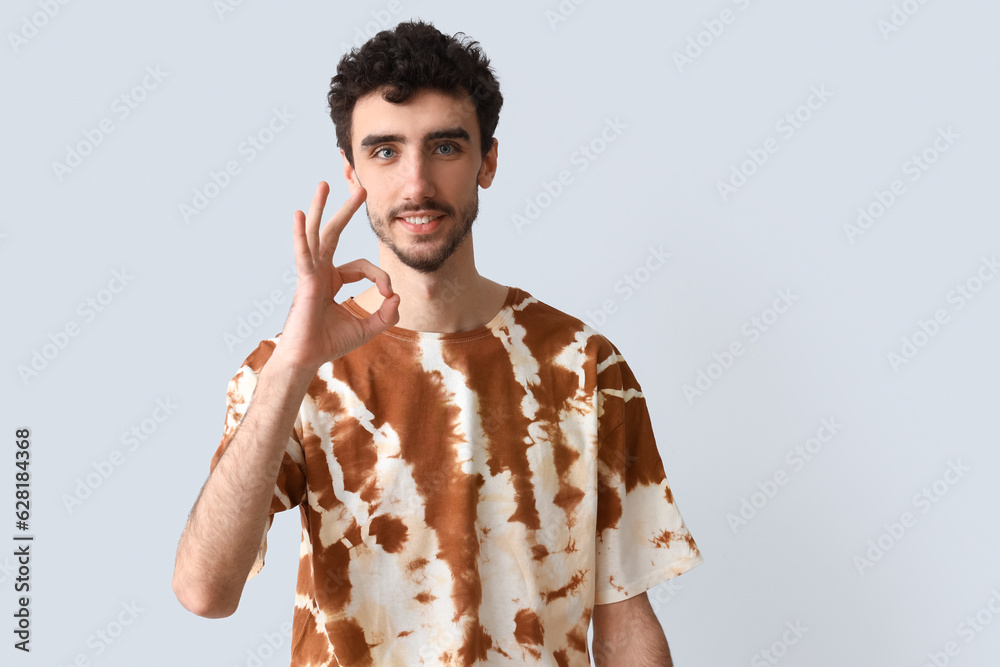 Handsome man in tie-dye t-shirt showing OK on light background