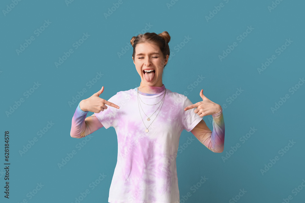 Young woman pointing at tie-dye t-shirt on blue background