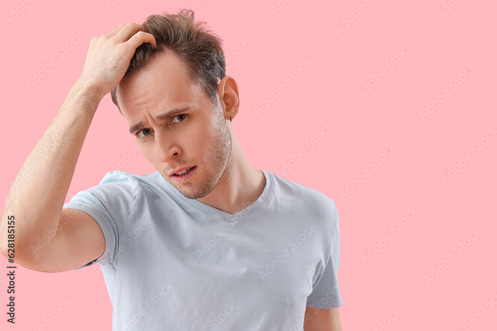 Upset young man with hair loss problem on pink background