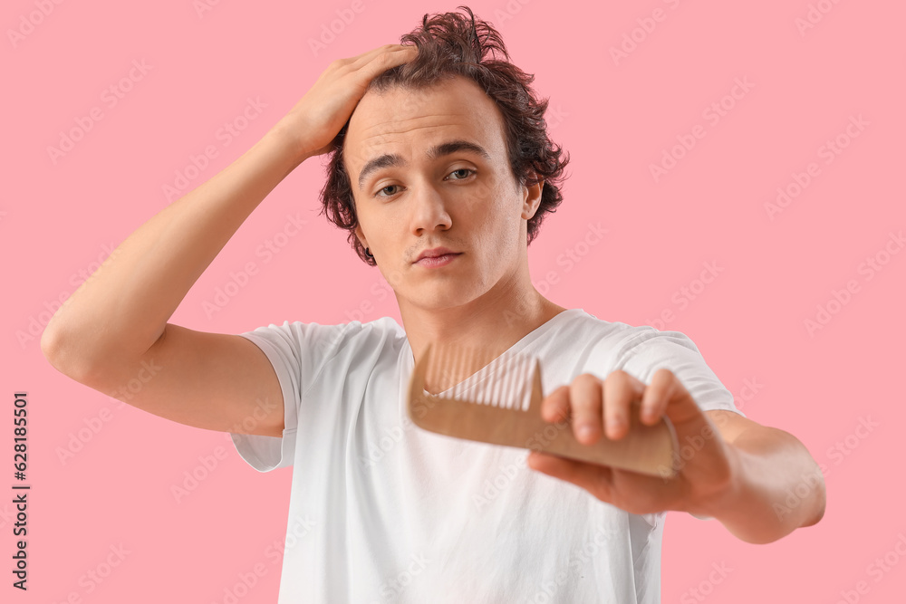 Young man with hair loss problem and comb on pink background