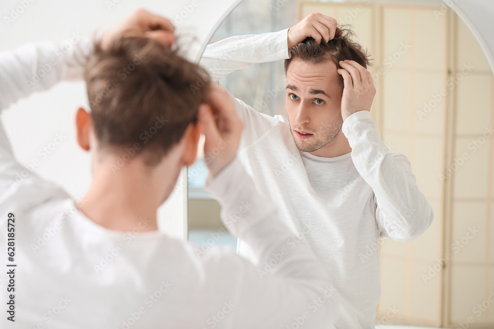 Young man with hair loss problem looking in mirror at home