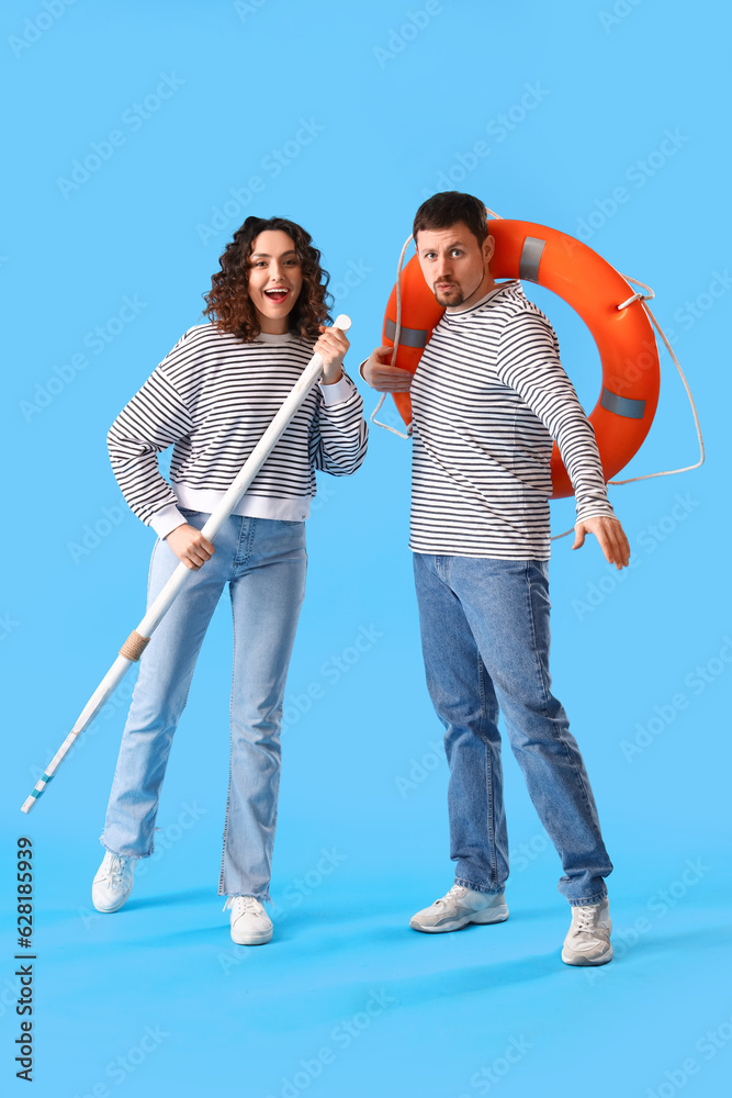 Young couple with paddle and ring buoy on blue background