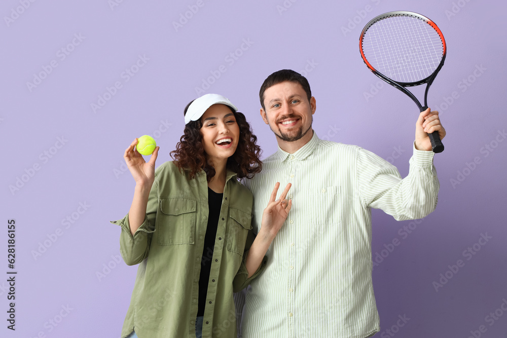 Young couple with tennis racket and ball on lilac background