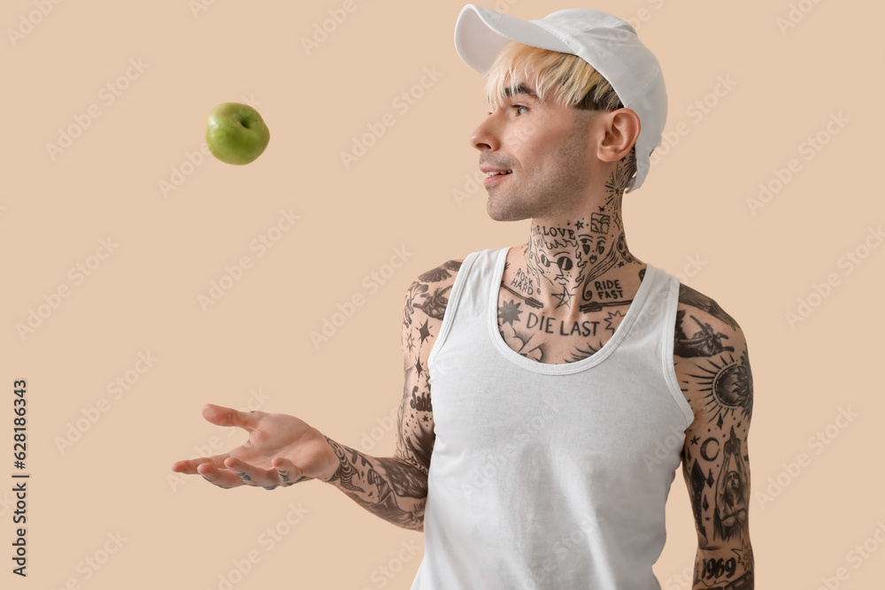 Tattooed young man with apple on beige background