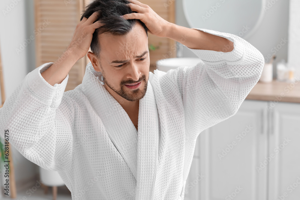 Worried young man with hair loss problem in bathroom