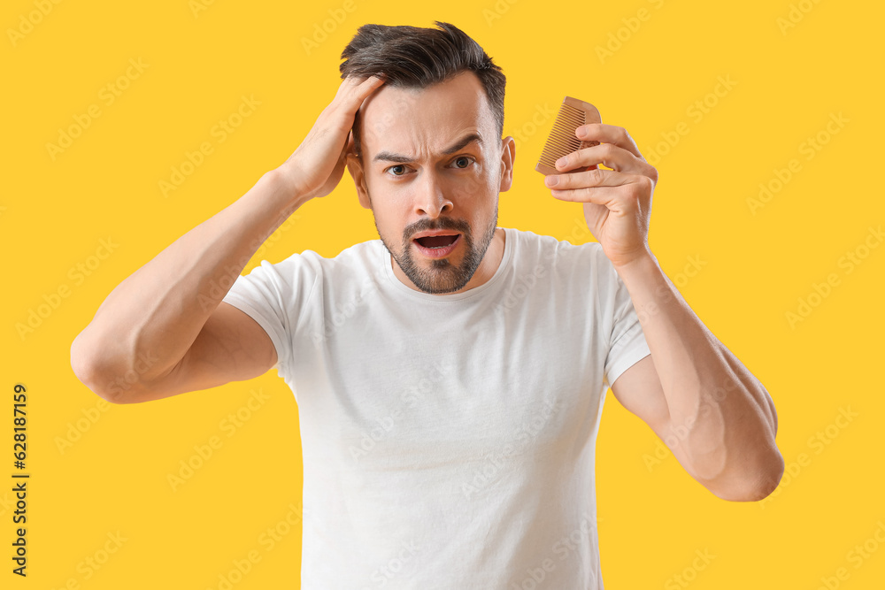 Worried young man with hair loss problem and comb on yellow background