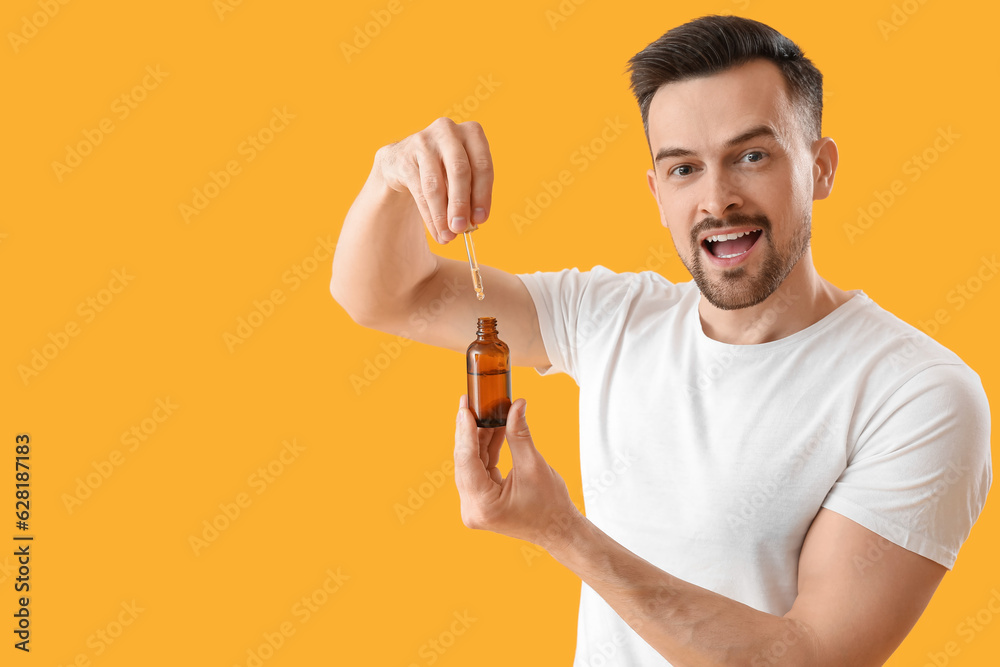 Handsome man with serum for hair growth on yellow background