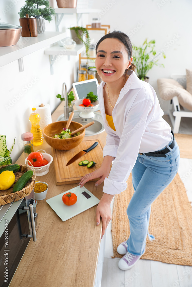 Young woman making vegetable salad in kitchen