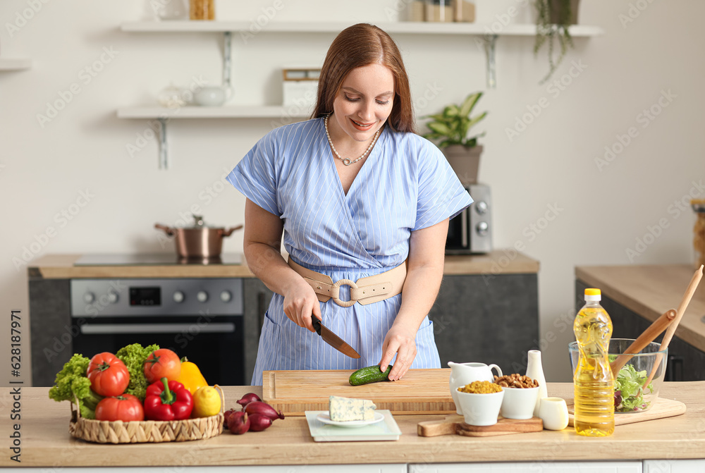 Young woman cutting cucumber for salad in kitchen