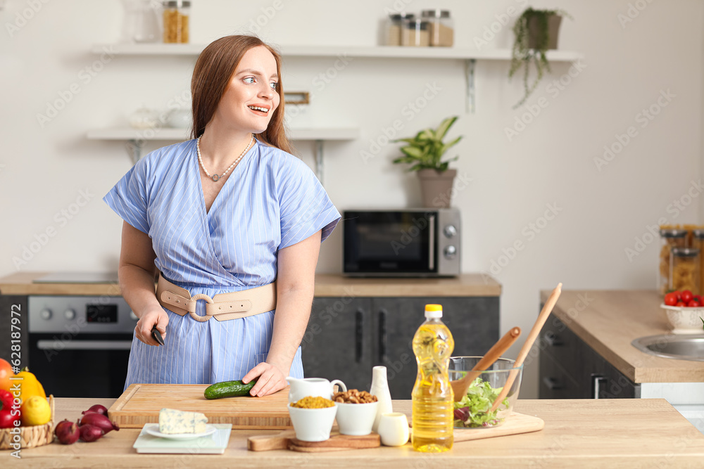 Young woman cutting cucumber for salad in kitchen