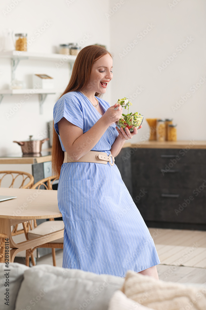 Young woman eating vegetable salad in kitchen