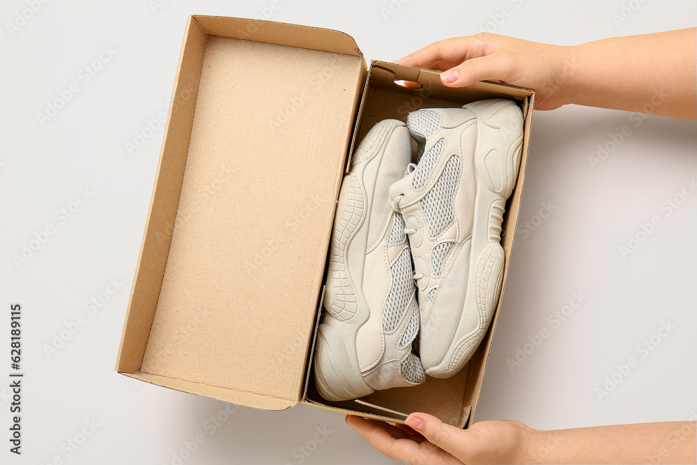 Female hands holding cardboard box with stylish shoes on beige background