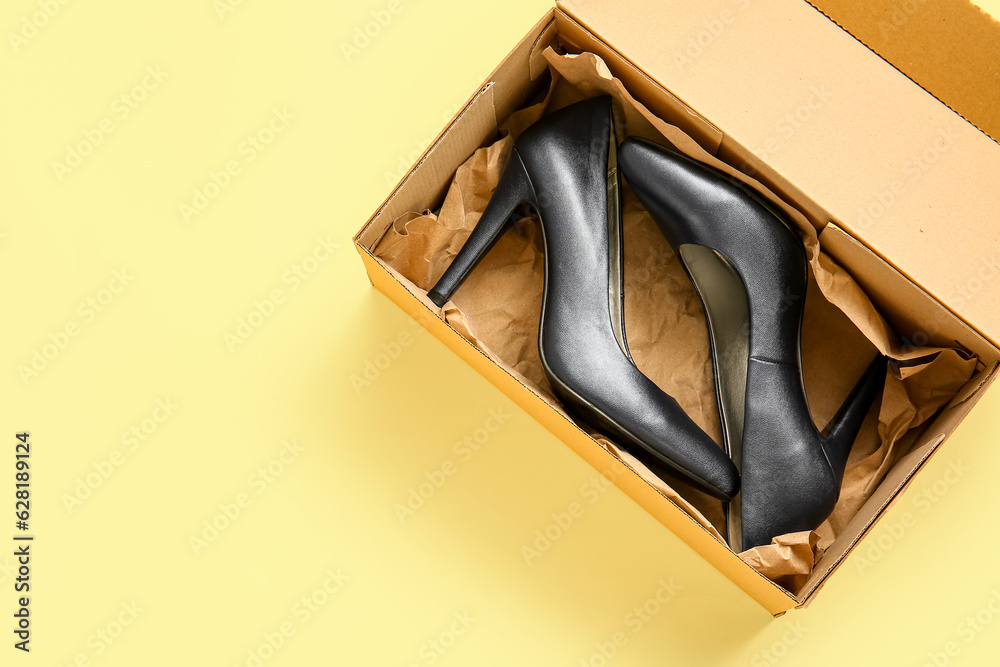 Cardboard box with high heeled shoes on beige background