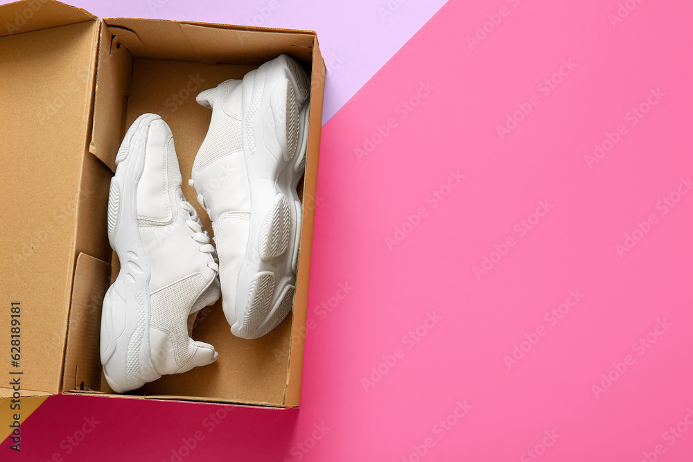 Cardboard box with sports shoes on color background