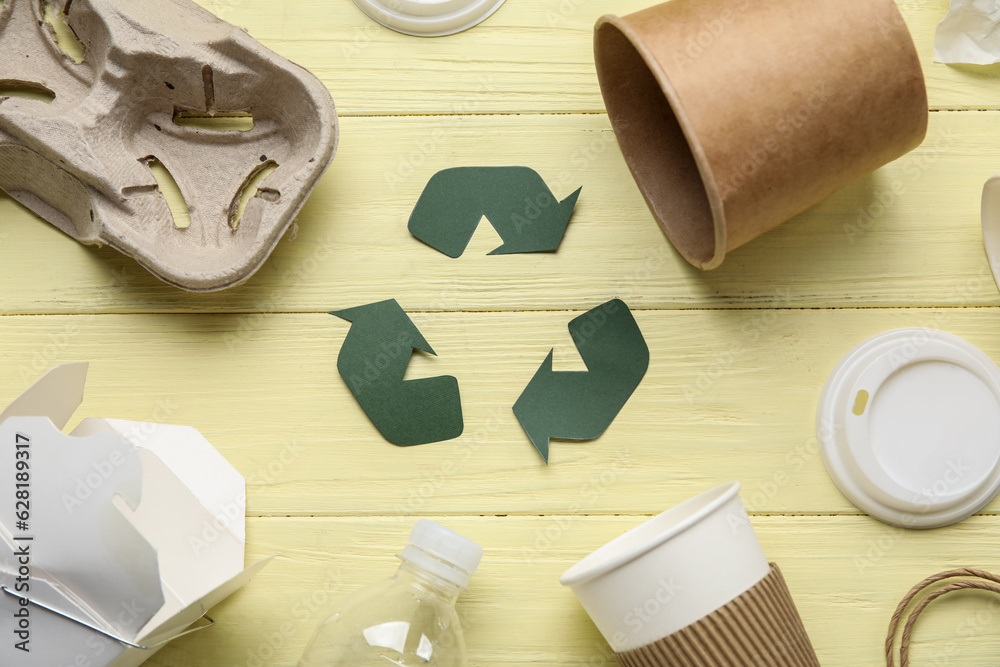 Recycling sign with garbage on yellow wooden background