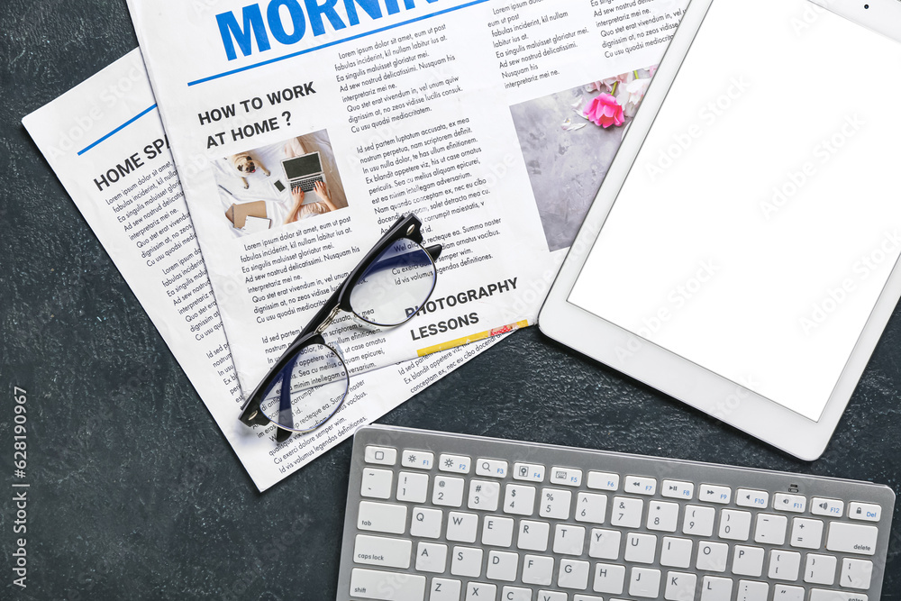 Tablet computer with newspapers, eyeglasses and keyboard on dark background