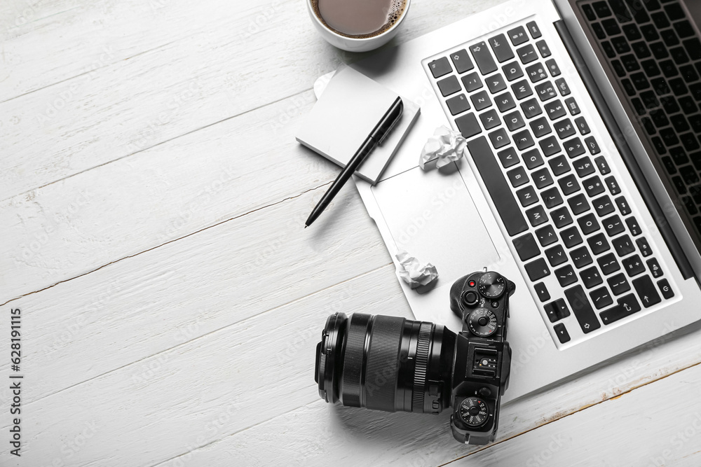 Laptop with sticky notes, photo camera, crumpled paper and coffee cup on white wooden background