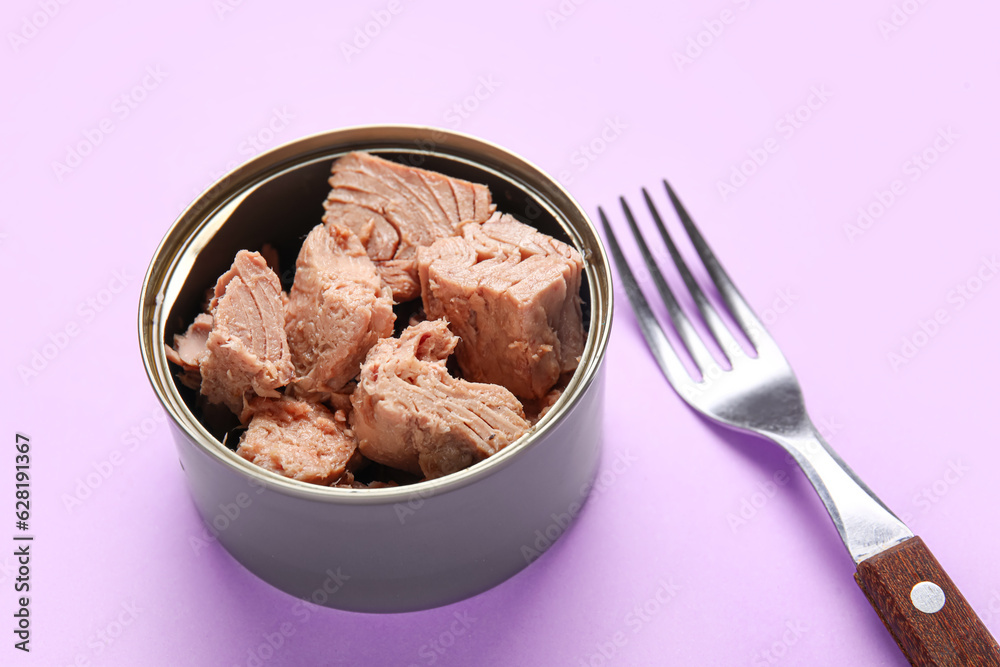 Opened tin can with delicious tuna and fork on lilac background